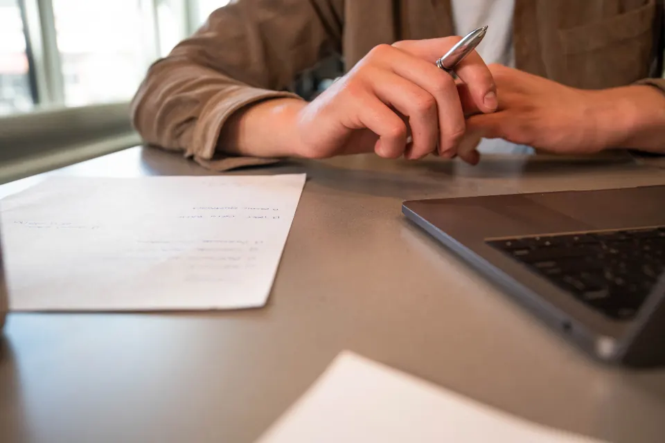 A person reading a printed page next to a laptop