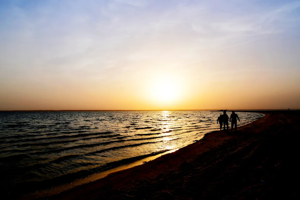 Two people walking along a beach at sunset